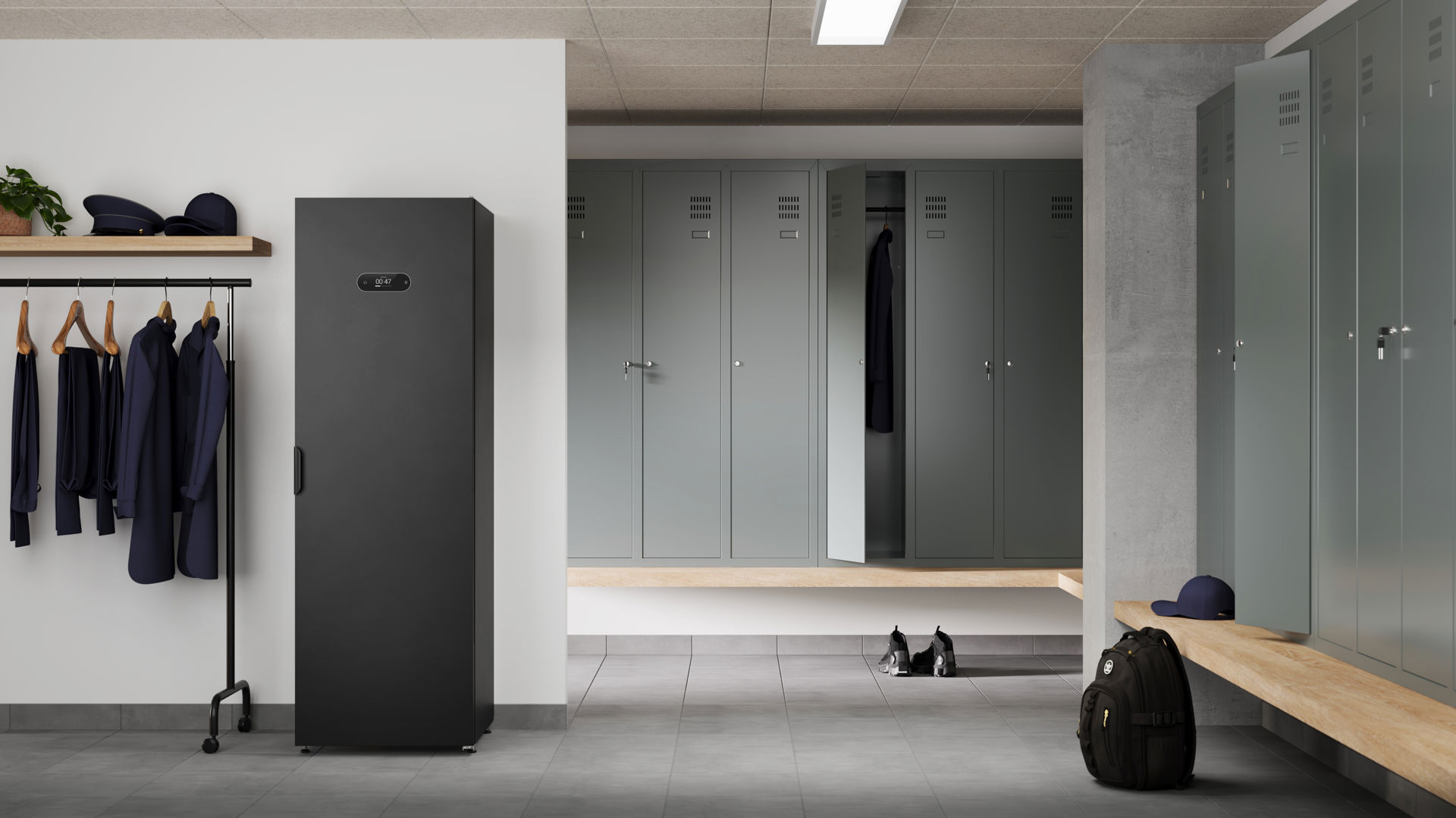 Det svarta Alizé Steaming Cabinet står i ett ljust och modernt omklädningsrum, omgiven av plåtskåp i en grågrön nyans.